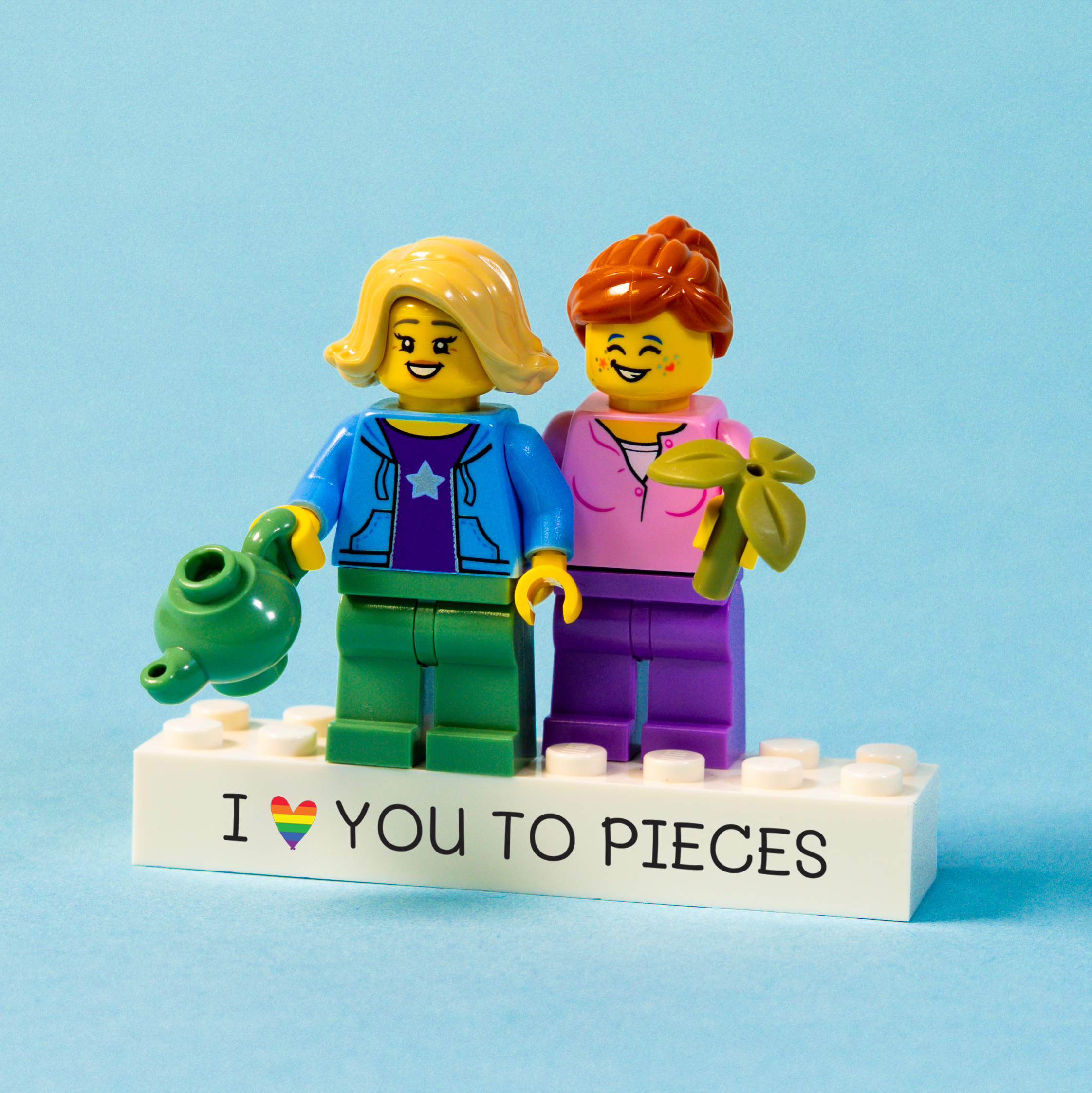 Two LEGO figures with a brick saying 'I ❤️ YOU TO PIECES' on a blue background