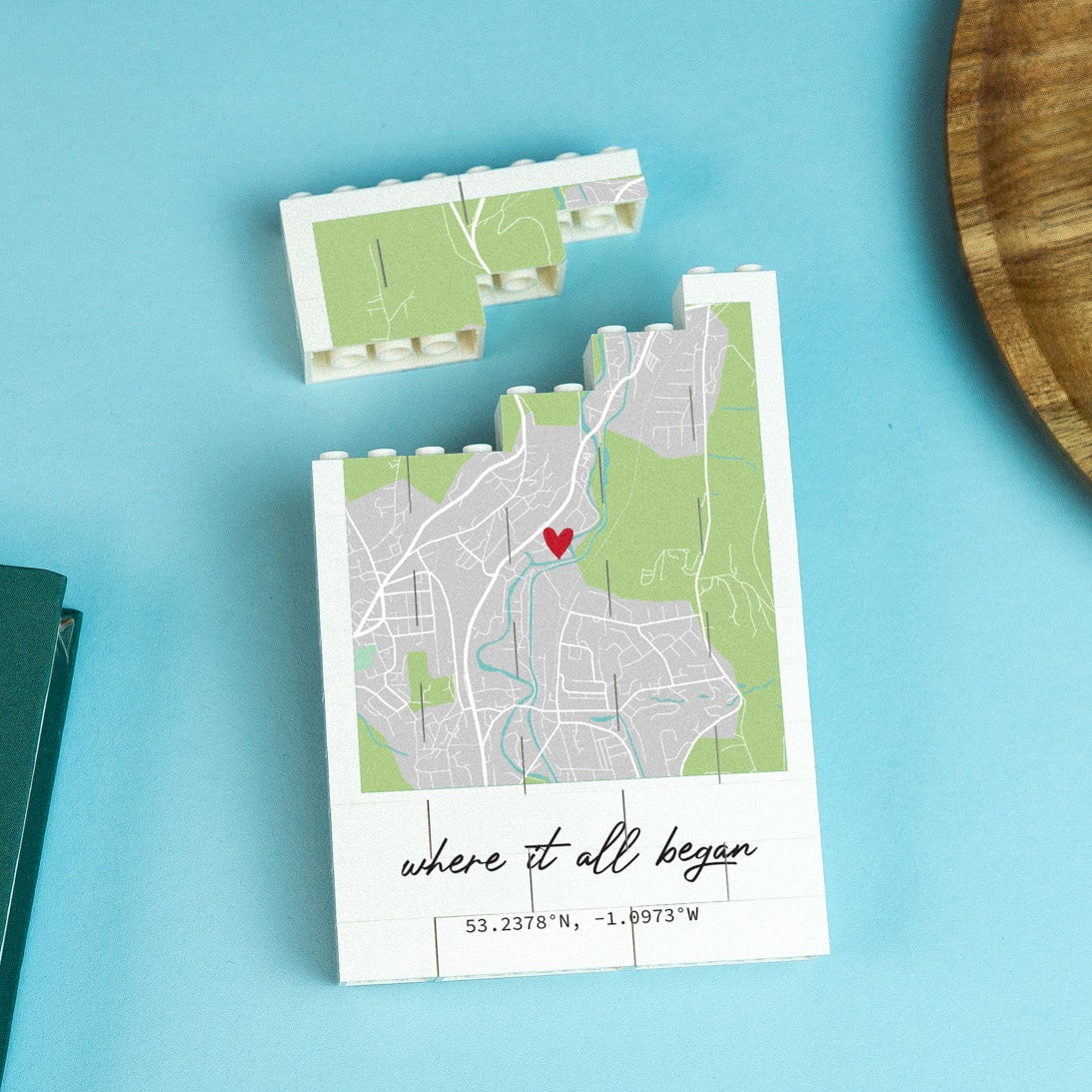 Small map with a heart symbol printed on LEGO® bricks on a blue surface next to a green planner and wooden plate.