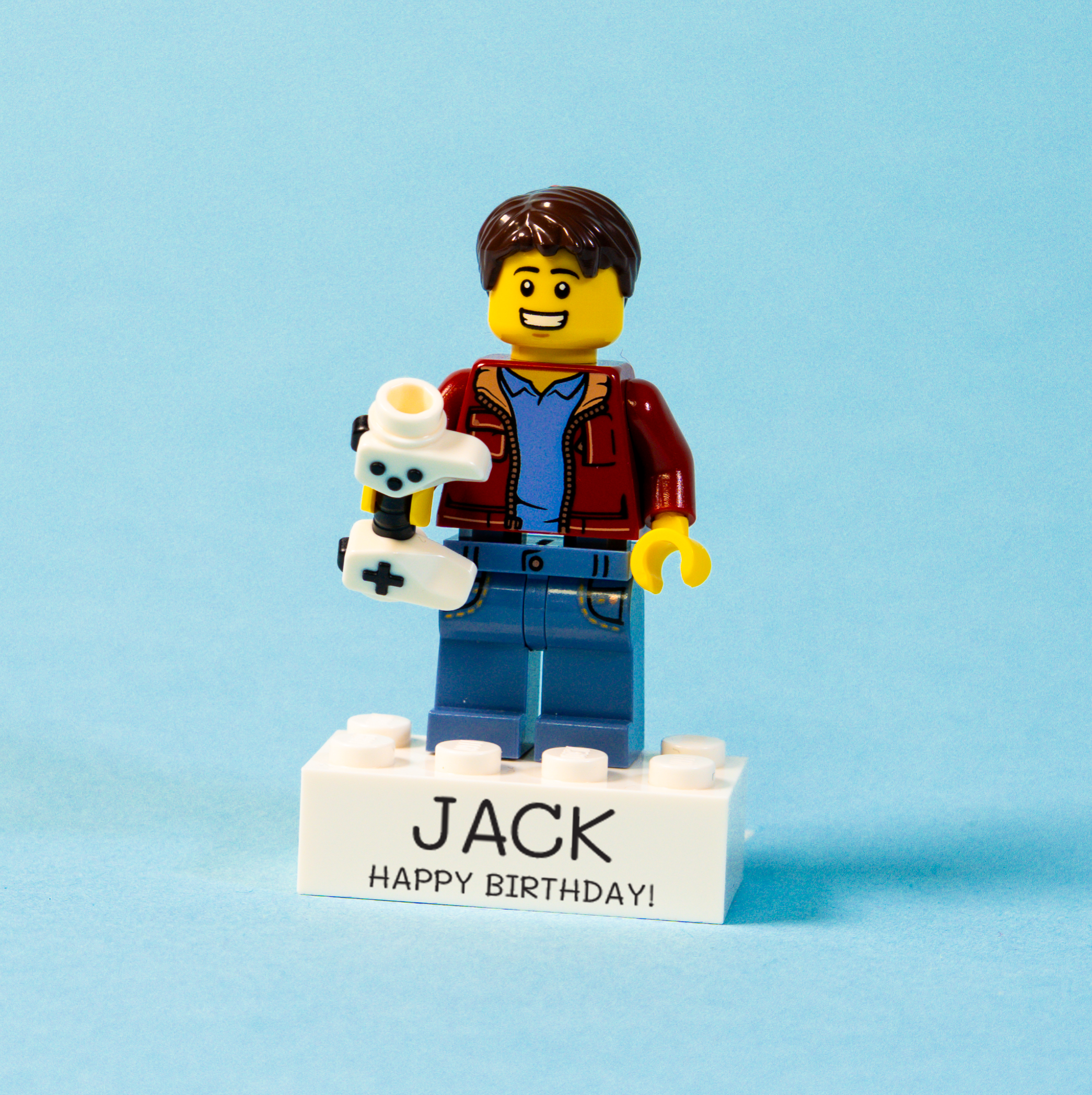 LEGO figure of a boy holding a games controller with 'Jack' and 'Happy Birthday!' text on a blue background