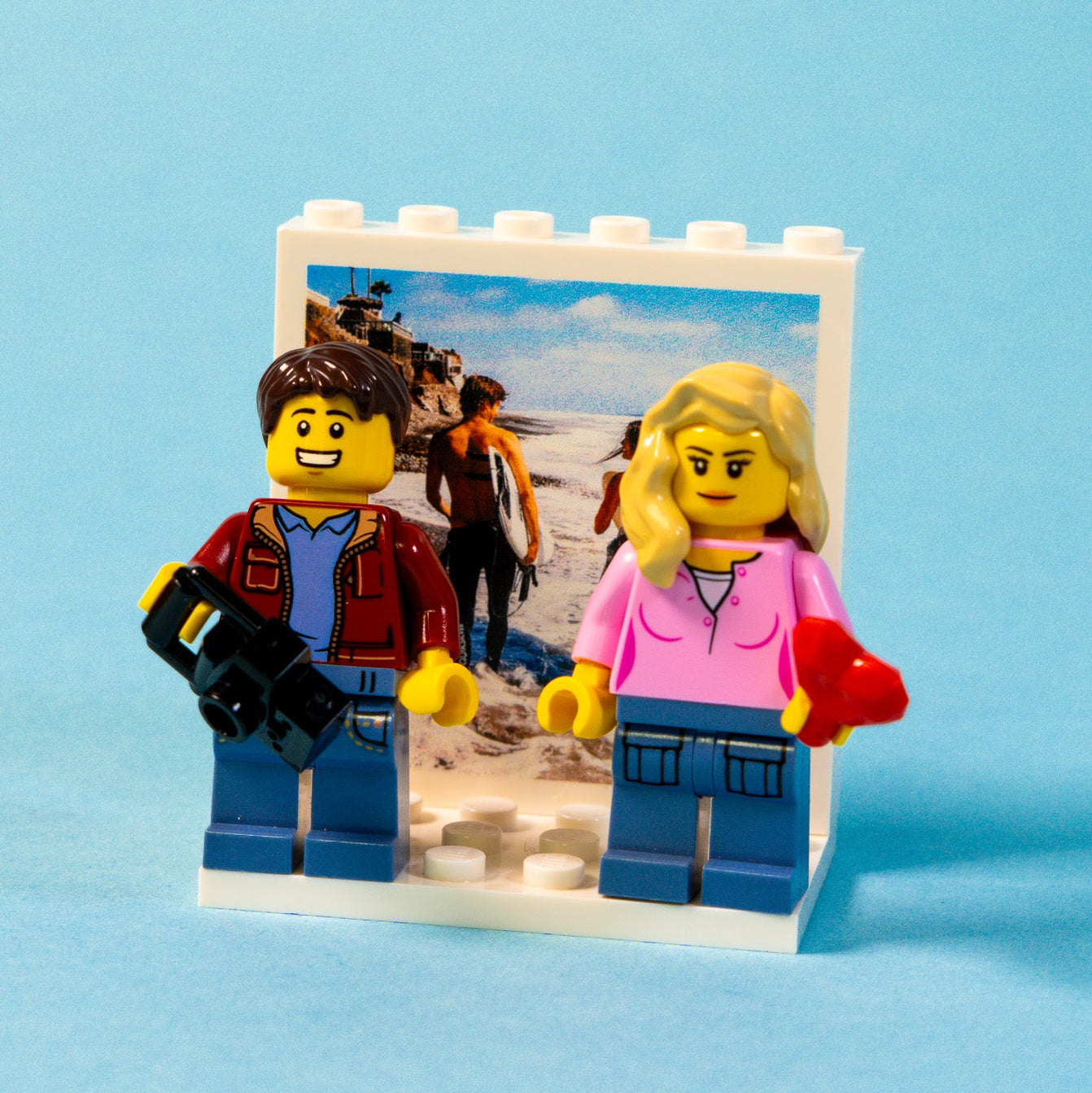 Two LEGO brick figures on a small platform with a personalised photo background on a blue background